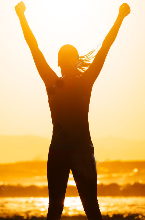 Fitness woman celebrating sport success on beautiful summer sunset or morning on the beach.  Successful female runner silhouette raising arms to the sun.